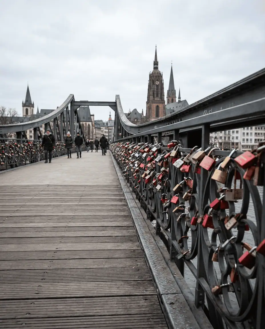A perspective shot looking down the Eiserner Steg footbridge, lined with thousands of colorful love locks, leading the eye towards the church spires of the Old Town.