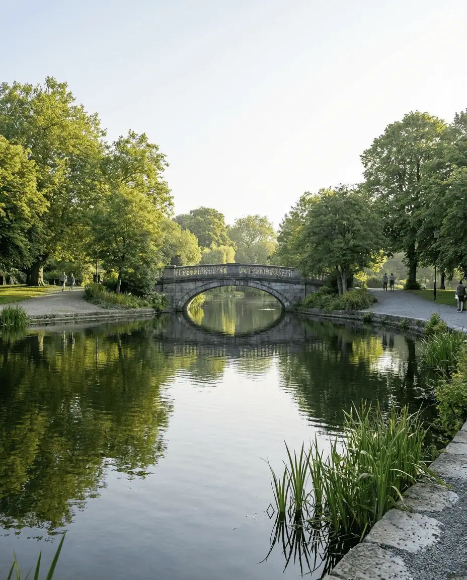 A peaceful landscape of St. Stephen's Green park, showing the ornamental lake, the stone bridge, and lush green trees in the heart of the city.