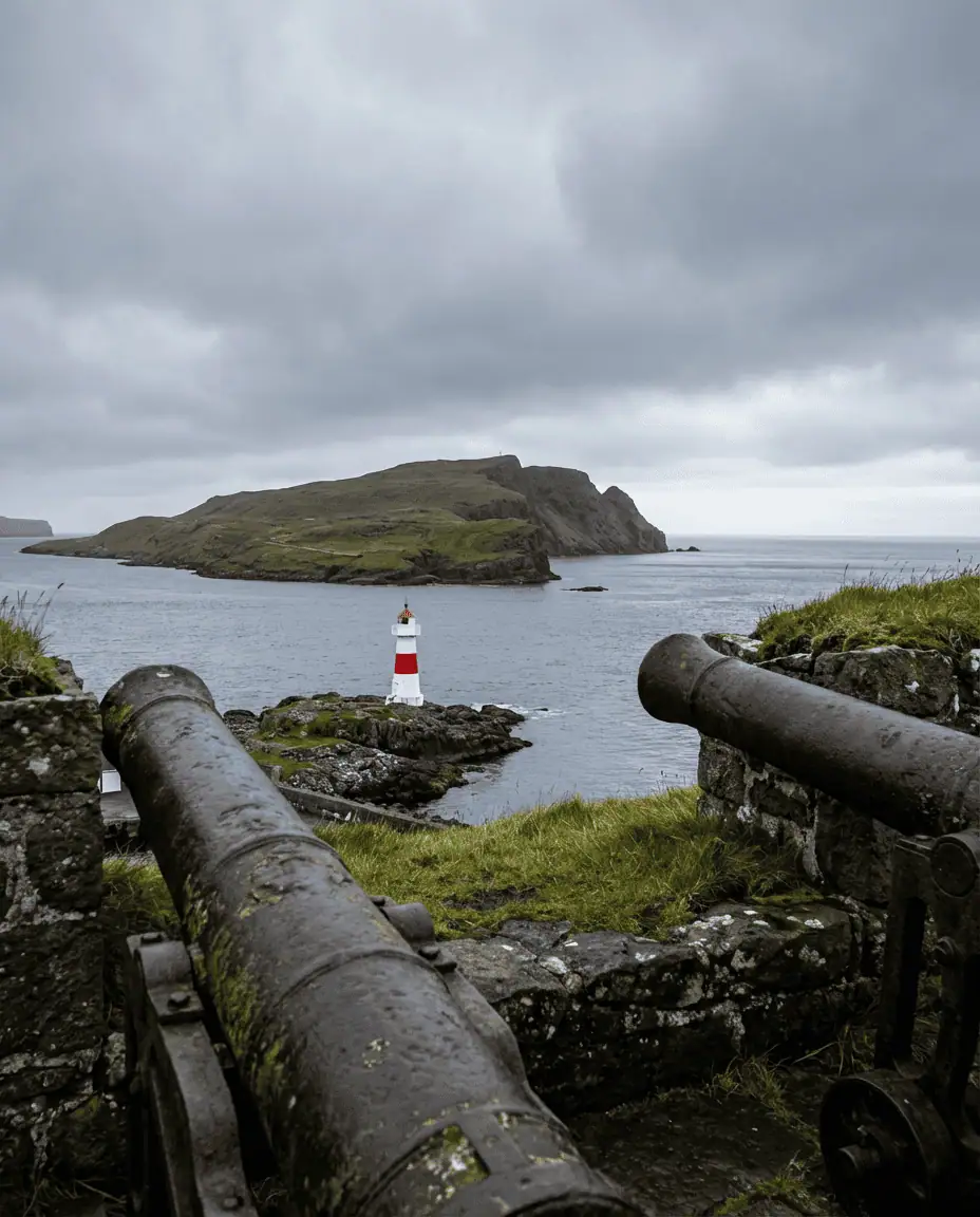 View from Skansin fortress looking out past the red-and-white lighthouse towards the island of Nólsoy, framed by old cannons