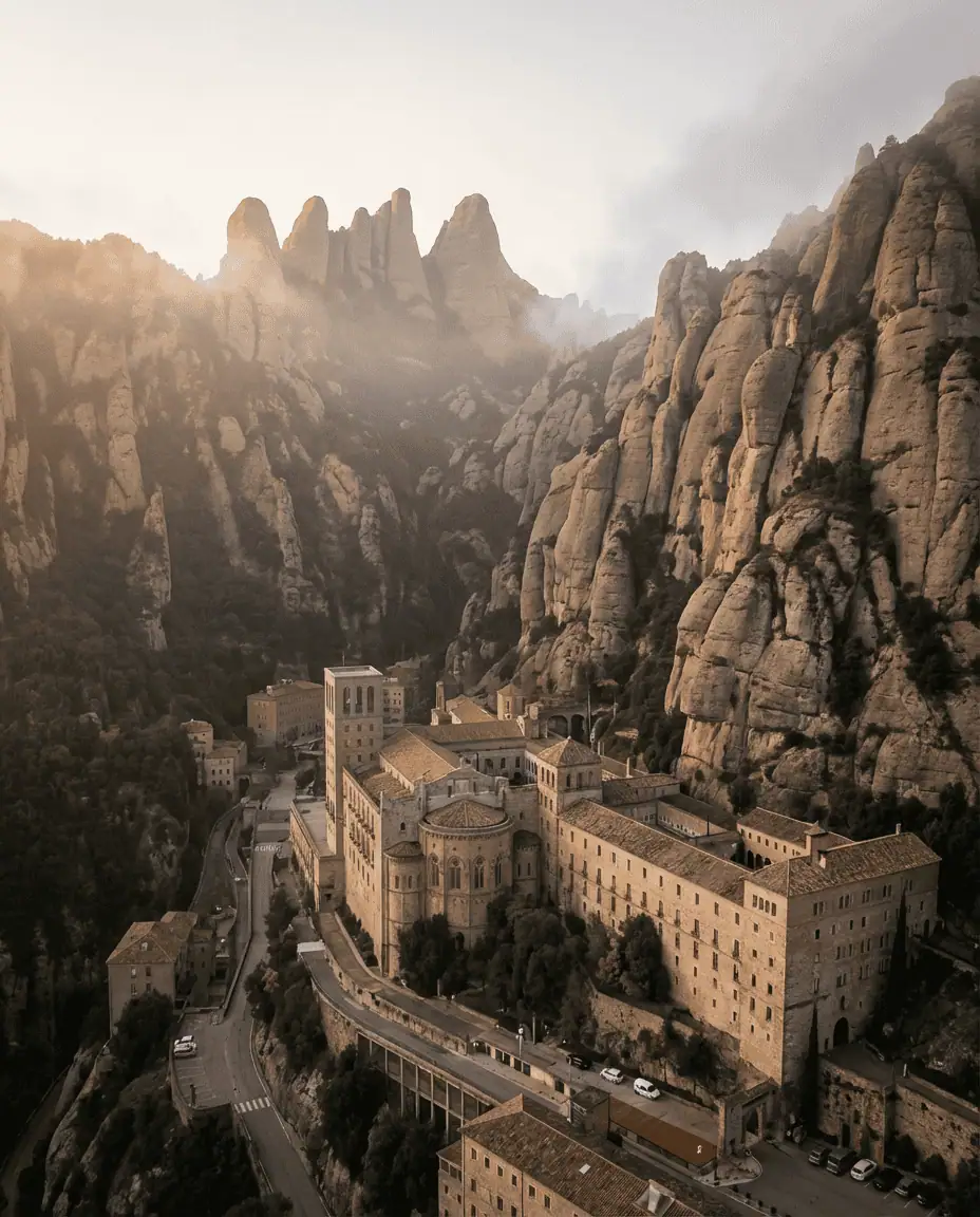 majestic wide shot of the Santa Maria de Montserrat Abbey nestled into the jagged, saw-toothed rock formations of the mountain