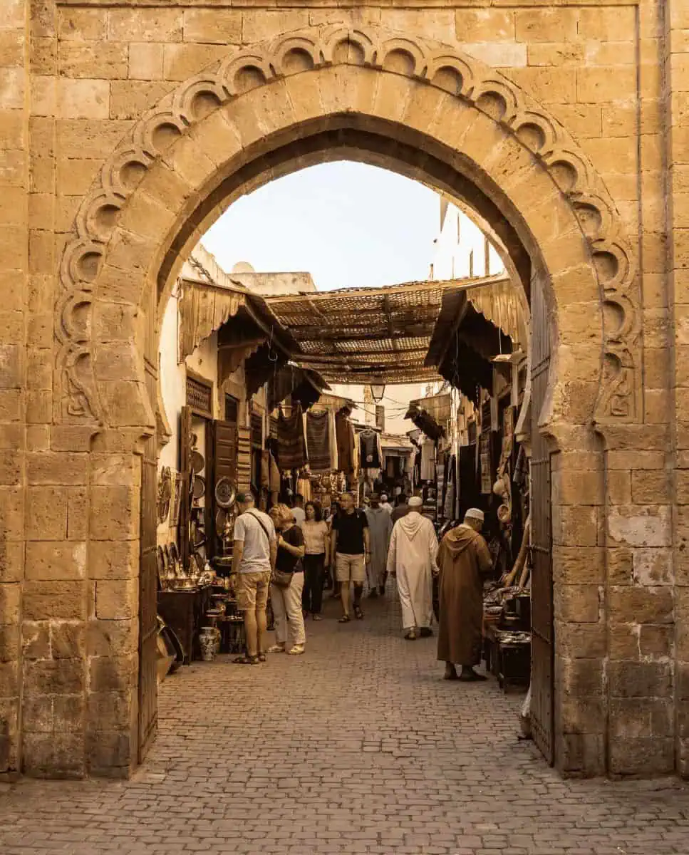 A picturesque view through a stone archway in the Habous Quarter, showing locals walking through a clean alleyway lined with traditional artisan shops.