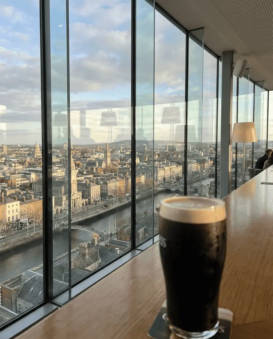 A panoramic view from the glass-walled Gravity Bar at the Guinness Storehouse, looking out over the Dublin skyline with a fresh pint of stout in the foreground.