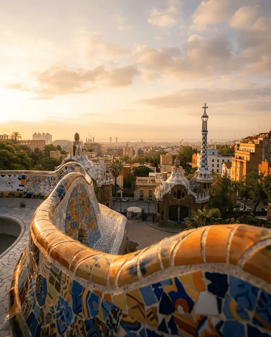 Atmospheric view from the mosaic serpentine bench at Park Güell at sunset, looking out over the gingerbread houses towards the distant sea