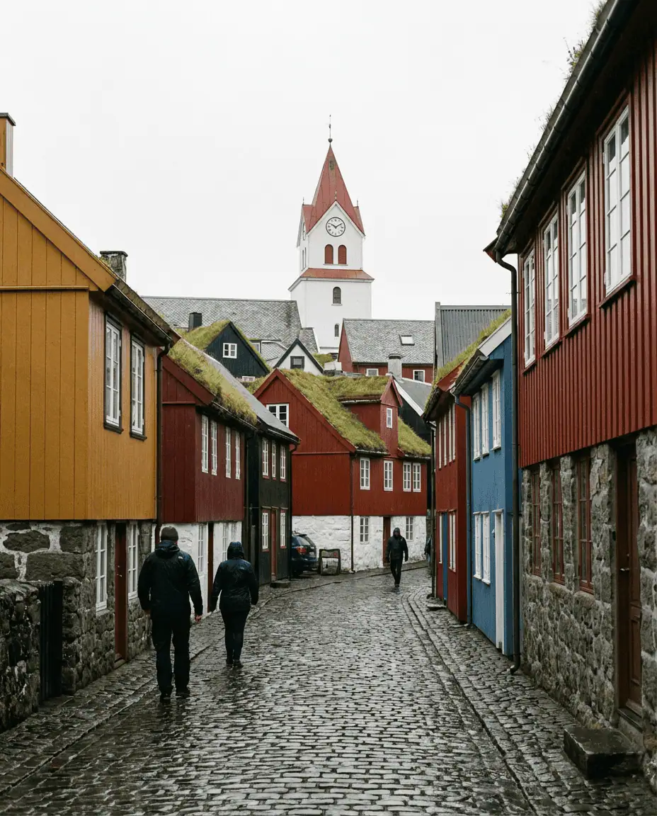 Street-level view of the white Tórshavn Cathedral clock tower rising above the narrow, colorful streets of the Old Town