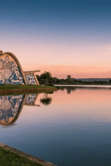 A stunning wide-angle shot of the Church of Saint Francis of Assisi in Pampulha, reflecting perfectly in the lake waters during a golden sunset, highlighting its modernist curves.