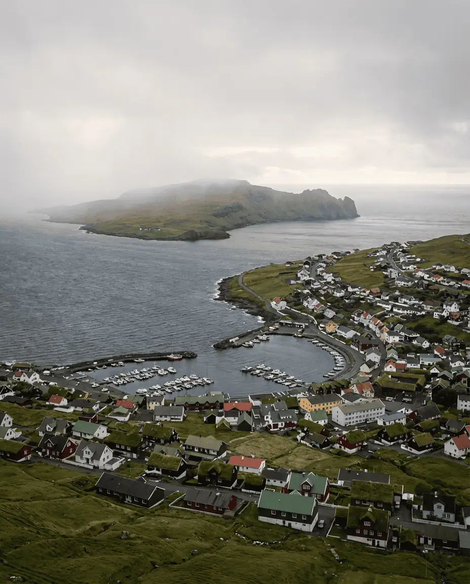 A panoramic wide shot taken from the Hotel Føroyar viewpoint, capturing the entire city of Tórshavn cascading down to the sea with the island of Nólsoy looming in the background.