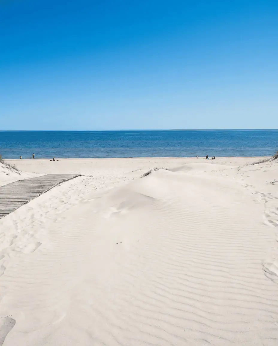 A sunny summer landscape of the white silica sand dunes at Grand Beach, with the blue waters of Lake Winnipeg stretching to the horizon.