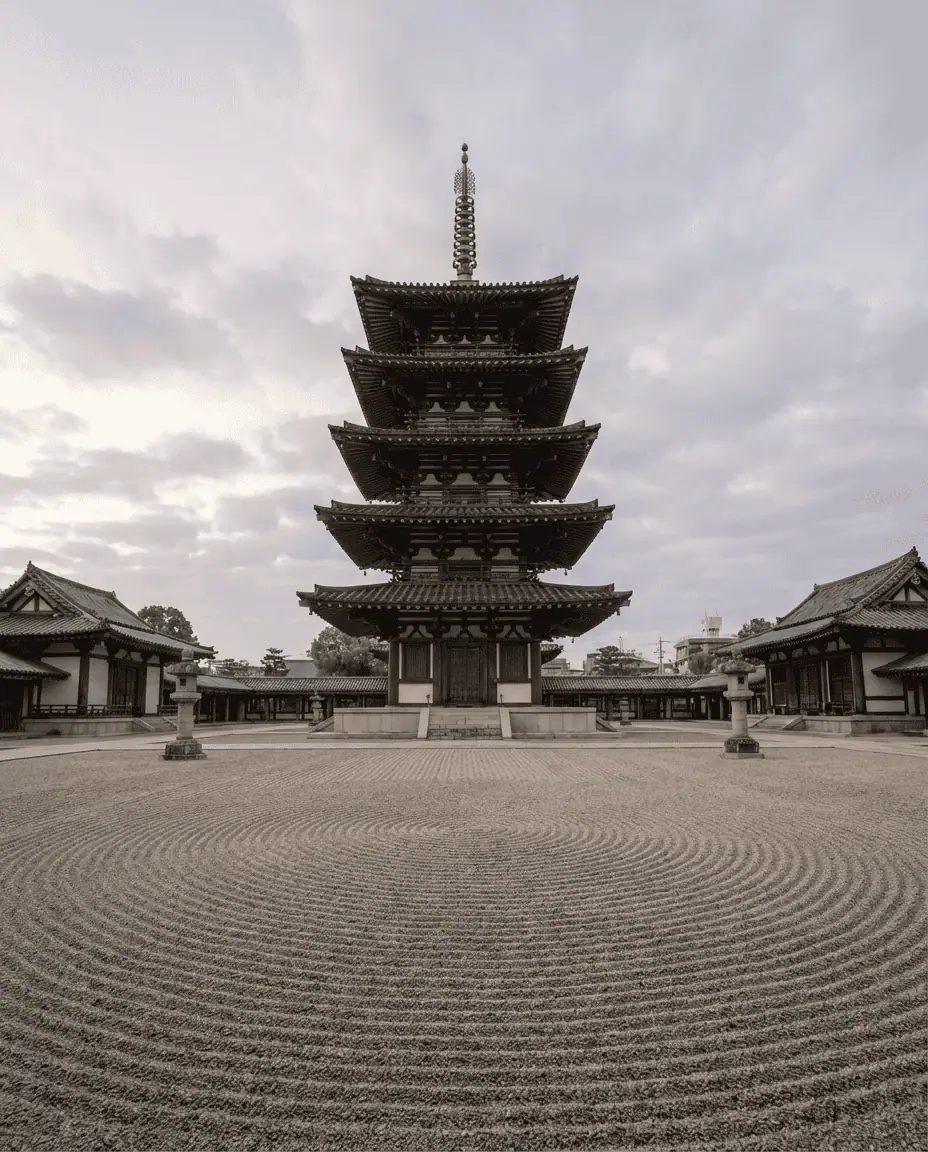A serene, wide shot of the five-story pagoda at Shitennoji Temple standing in the center of a raked gravel courtyard, emphasizing the ancient symmetry and calm.