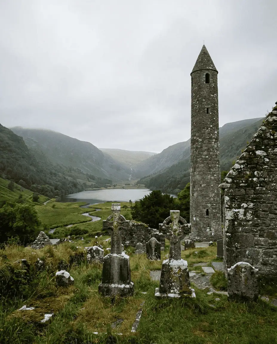 A serene shot of the ancient stone Round Tower and cemetery at Glendalough, nestled in a green valley with the Wicklow Mountains in the background.